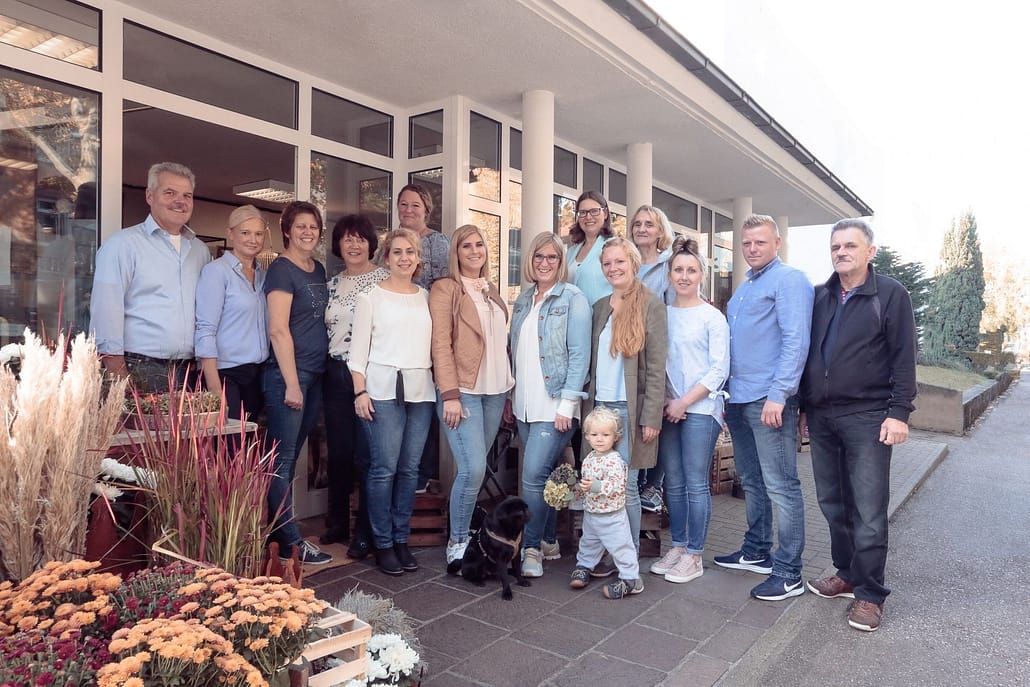 Teamfoto der Gärtnerei Reinwald mit mehreren Personen und blühenden Pflanzen im Vordergrund.