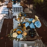 Lange Holztischtafel mit blauen Hortensien, gelben Blumen, Zitronen und gestreiften Läufern
