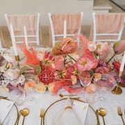 Bunte Tischdekoration mit Blumen in Rosa und Lila, Glasvasen und weißen Kerzen.