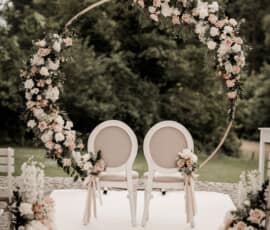 Traubogen mit weißen und roséfarbenen Rosen, Grün und zwei Stühlen für eine freie Trauung im Freien.