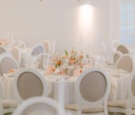 Festlich gedeckte Hochzeitstische mit apricotfarbener Blumendekoration und üppigem Blumenschmuck an der Decke.
