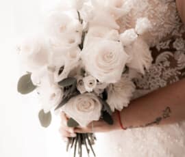 Braut hält einen eleganten weißen Brautstrauß mit Rosen, Calla und zartem Grün von der Gärtnerei Reinwald.
