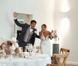 Brautpaar betritt überrascht den festlich dekorierten Hochzeitssaal mit Blumenschmuck in Weiß- und Naturtönen.