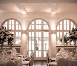 Elegante Hochzeitslocation mit runden Tischen und hohen weißen Blumengestecken von Gärtnerei Reinwald Heilbronn.