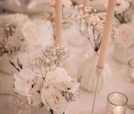 Romantische Hochzeitstischdekoration mit weißen Rosen, Schleierkraut und brennenden Stabkerzen.