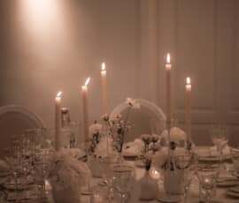 Stimmungsvoll gedeckte Hochzeitstafel mit weißen Blumen, hohen Kerzen und floraler Deckendekoration.
