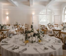 Runde Hochzeitstische mit weißer Blumendekoration, Eukalyptus, Kerzen und Zitronen in heller Festlocation.