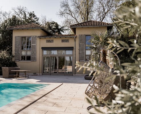 Gartenvilla mit Pool, großen Fenstern und umliegenden Bäumen, moderner Architektur und klaren Linien.